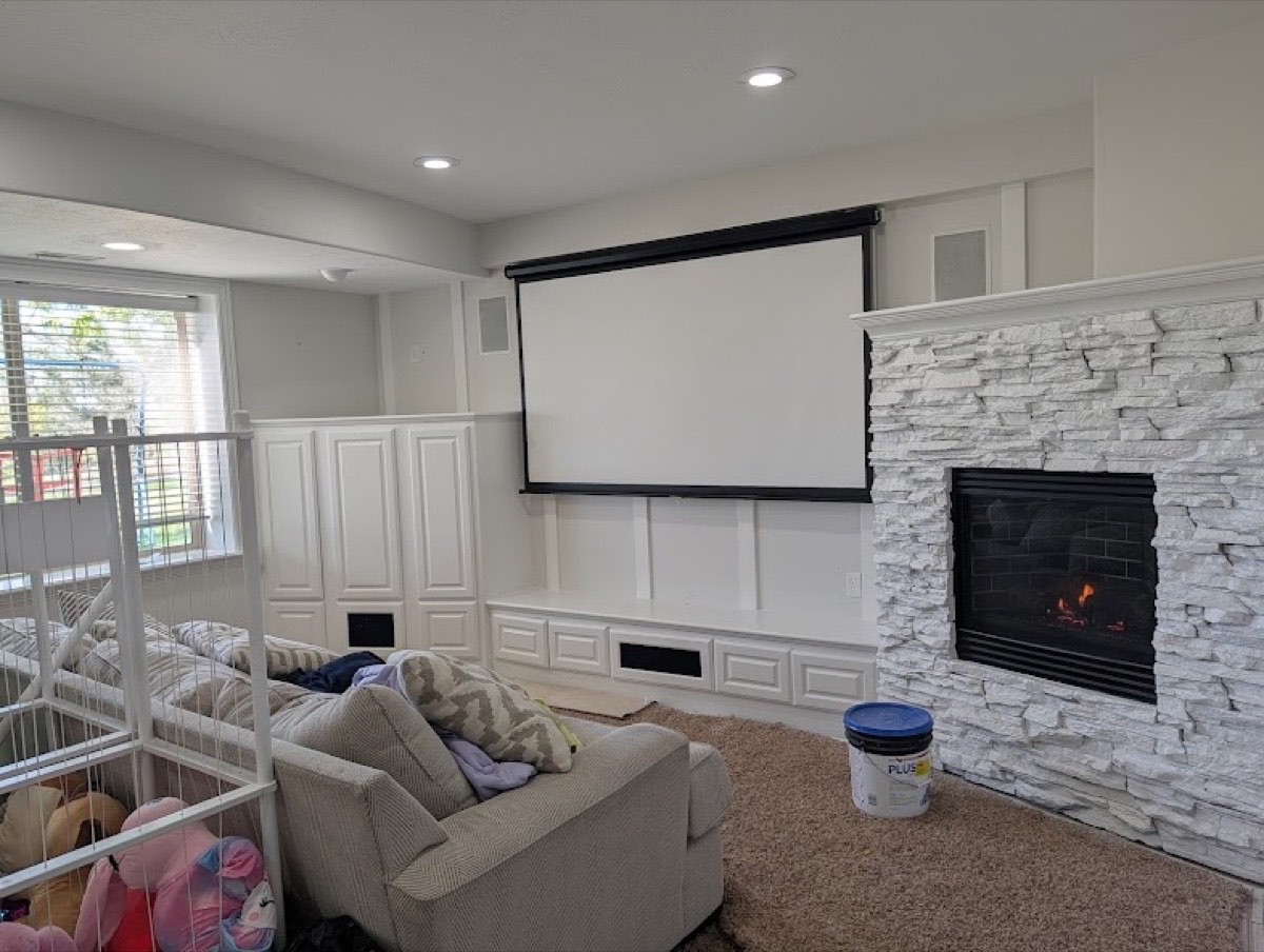 Finished basement theater room with stacked-stone fireplace, white wainscoting, and built-in cabinets painted by Budget Painting LLC in Utah County